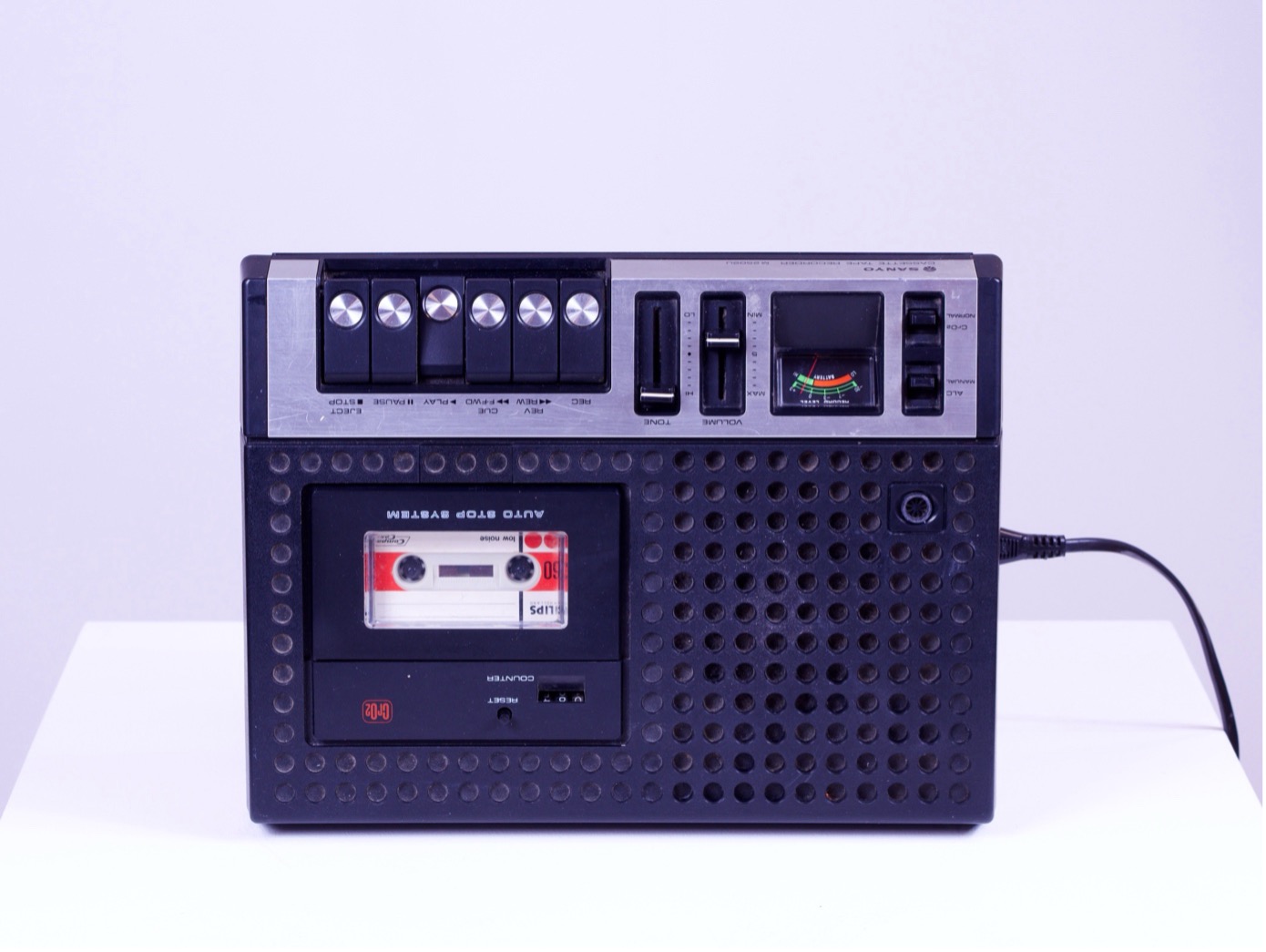Magnétophone à cassette SANYO des années 1970 posé sur un socle blanc, une cassette Philips dans le compartiment