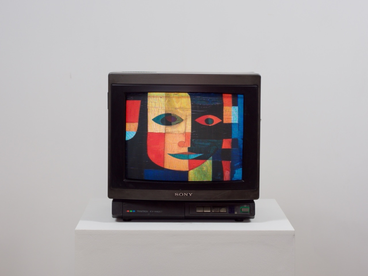 Téléviseur cathodique Sony Trinitron sur un socle blanc, affichant un visage abstrait en aplats de couleurs