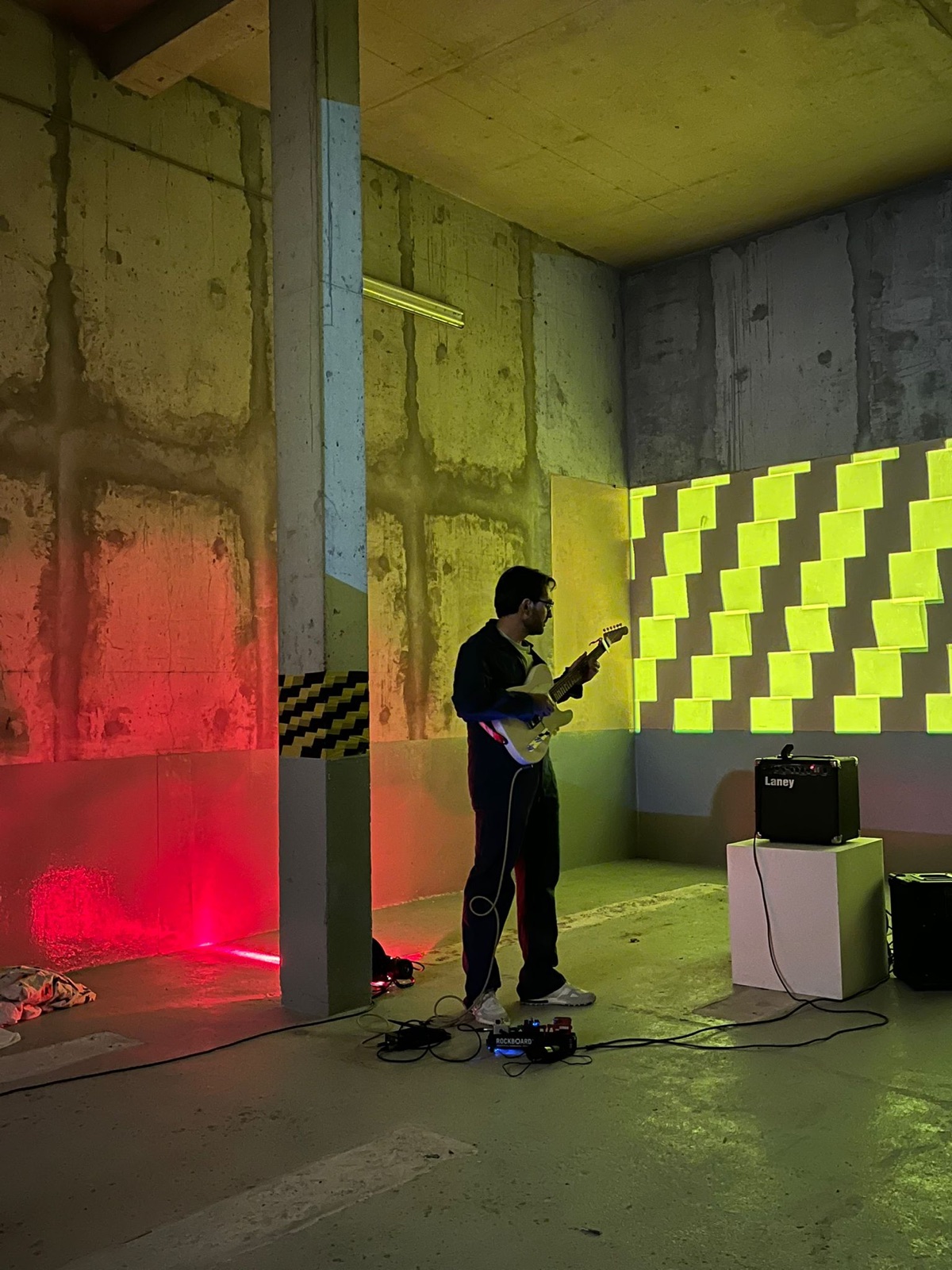 Guillaume Milochau à la guitare dans le sous-sol, lumière rouge à gauche, damier jaune projeté à droite