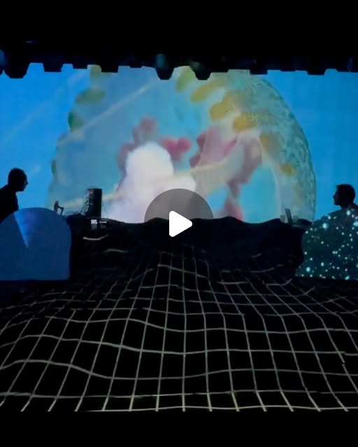 Concert live-mapping : deux musiciens en silhouette devant une projection sous-marine, une grille lumineuse au sol
