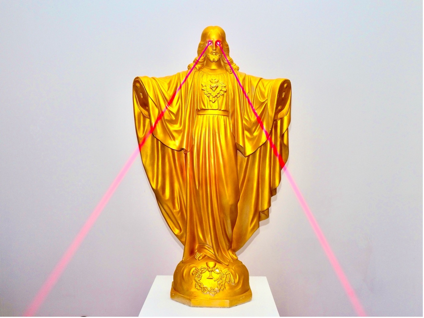 Statue dorée sur un socle blanc, bras ouverts, émettant des faisceaux laser roses depuis les yeux